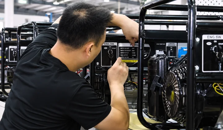 A worker positions a model label on an open-frame generator control panel