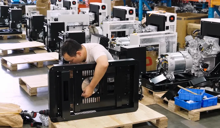 Worker assembling a generator enclosure with engine and alternator assemblies visible