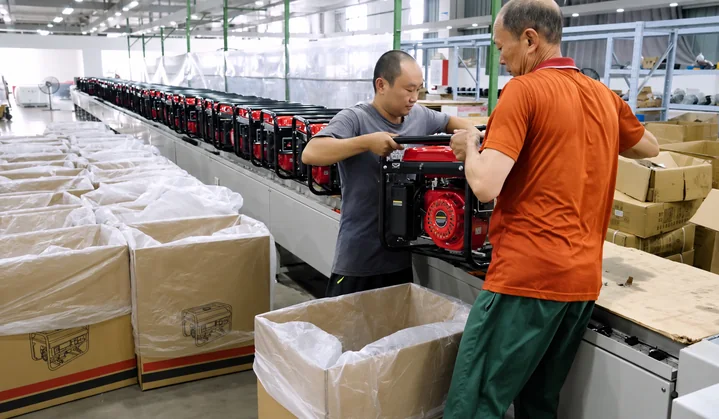 Two workers position an open-frame generator above a lined shipping carton