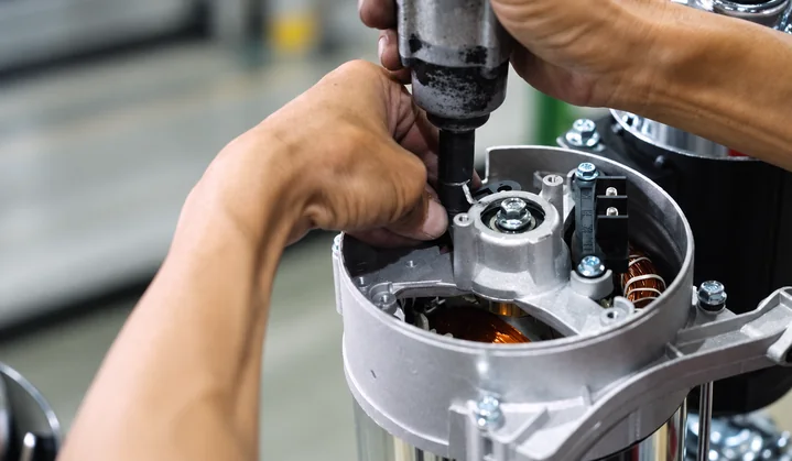 Close-up of a worker using a handheld tool on a cylindrical component assembly