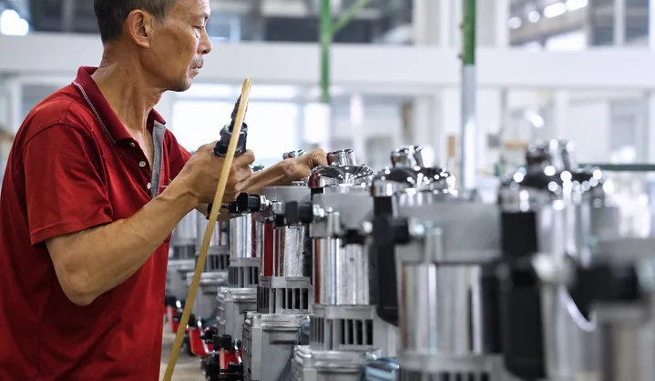 A worker uses a handheld tool beside a row of cylindrical component assemblies